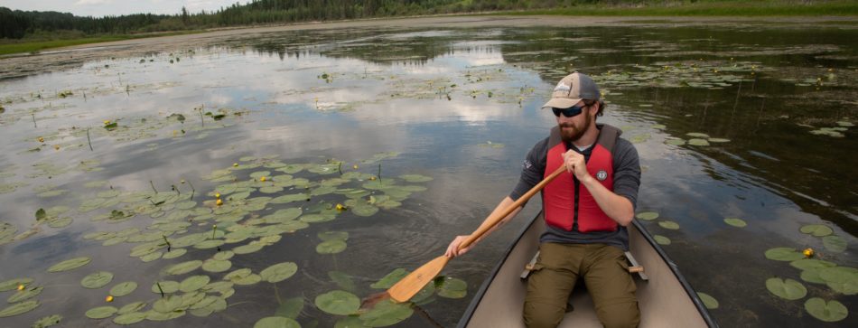 A man paddles a canoe on the still waters of Battle Lake